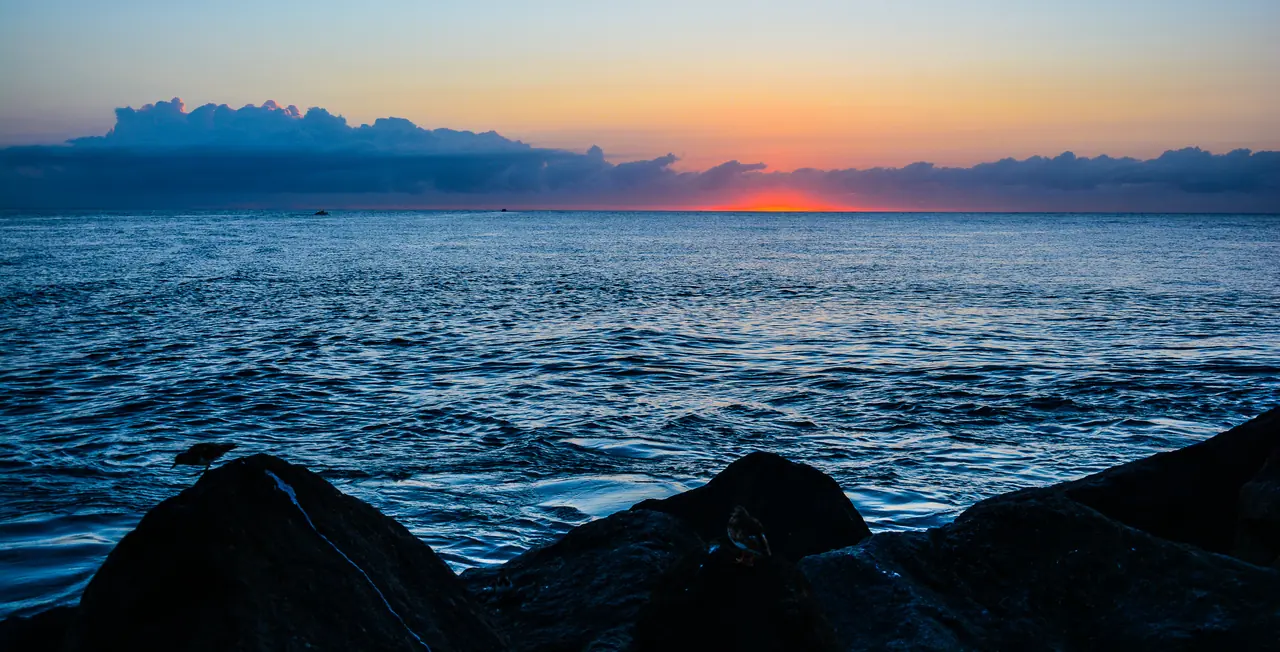 Lever de soleil sur la Méditerranée, rochers au premier plan et nuages à l'horizon